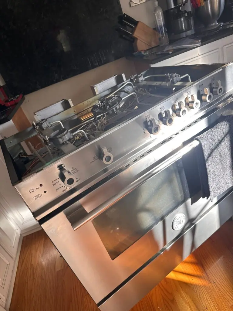 Stainless steel gas range with the oven door open during a repair