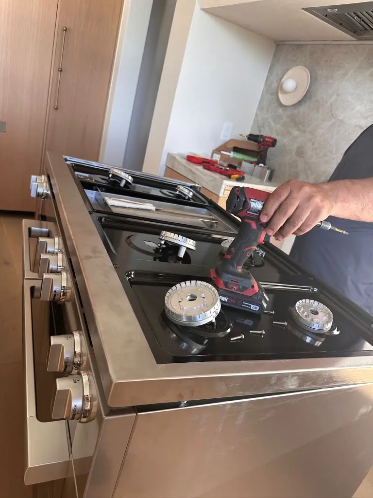 Technician repairing the burners of a gas cooktop with a power tool